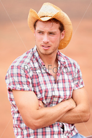 Cowboy man handsome and good looking with hat in rural USA countryside. Male model in american western prairie landscape nature on ranch or farm in USA.