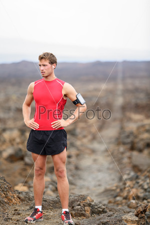 Runner man - portrait of running athlete resting after cross country run on trail. Fit handsome male triathlete taking break standing relaxing in beautiful volcano landscape on Big Island, Hawaii, USA