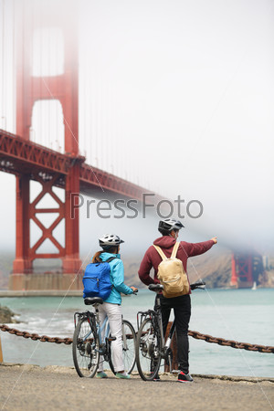 Golden gate bridge - biking couple sightseeing in San Francisco, USA. Young couple tourists on bike tour enjoying the view at the famous travel landmark in California, USA.
