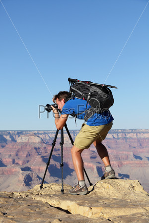 Nature landscape photographer in Grand Canyon taking picture photos with SLR camera and tripod during hike on south rim. Young man hiker enjoying landscape in Grand Canyon, Arizona, USA.