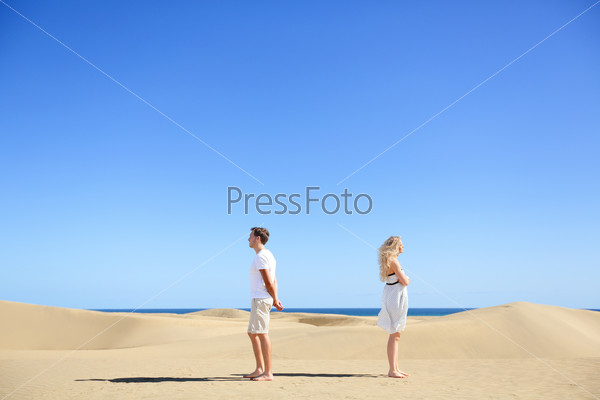 Relationship problem - upset couple argument. Angry couple in disagreement divorce and separation concept. Young couple with marriage problems. Woman and man conceptual image in desert under blue sky.