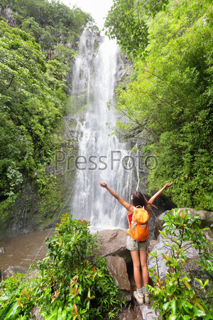 Happy hiker - Hawaii tourists hiking by waterfall. Woman cheering during travel on the road to Hana on Maui, Hawaii. Ecotourism concept image with happy female hiker.