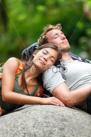 Hiking couple lovers relaxing sleeping in nature. Tired hikers resting lying down outdoors taking a break from hike. Young Asian woman and Caucasian man.