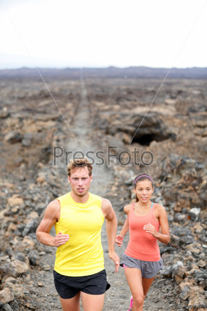 Trail running man and woman cross country runners jogging training outdoors for marathon run in beautiful volcano landscape nature. Couple, male and female athletes working out on Big Island, Hawaii.