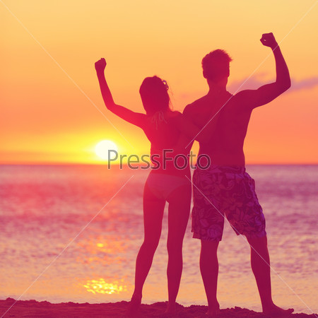 Winning success concept - happy beach couple at sunset with arms raised up outstretched cheering and happy. Beautiful young fitness couple, man and woman.