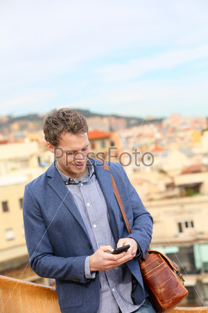 Young urban businessman professional using smartphone using app texting sms message on smart phone wearing trendy suit jacket in Barcelona, Catalonia, Spain. Caucasian male fashion model.