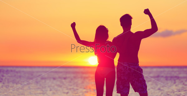 Happy fitness people on beach at sunset flexing showing muscles. Cheering winning couple expression joy and success together embracing. Man and woman on tropical beach.