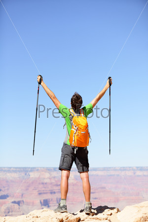 Celebrating success winner hiker cheering happy. Man hiking reaching Grand Canyon south rim summit goal. Young fit strong man with arms raised up holding hiking poles.