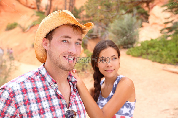 Couple portrait in american countryside outdoors. Smiling multiracial young couple in western USA nature. Man wearing cowboy hat and woman wearing USA flag shirt.