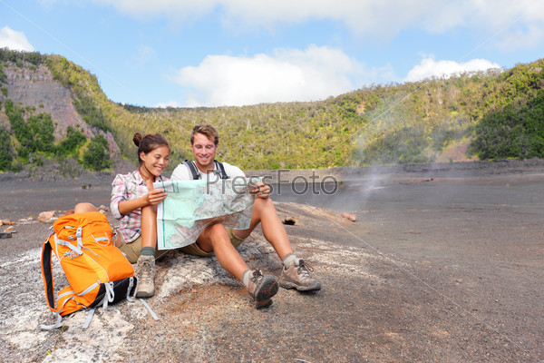 Couple hiking on volcano on Hawaii looking at map. Happy young man and woman relaxing taking break in beautiful volcanic landscape nature on Big Island in Hawaii Volcanoes National Park, USA.