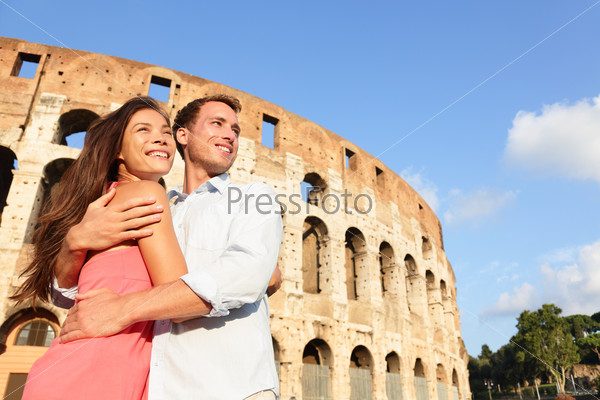 Romantic travel couple in Rome by Coliseum embracing in Italy. Happy lovers on honeymoon sightseeing having fun in front of Colosseum. Love and travel concept with multiracial couple.
