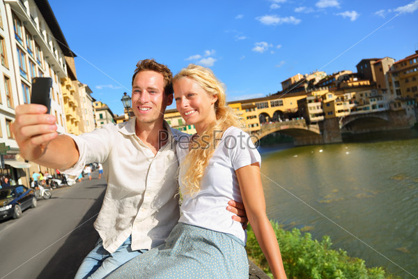 Happy couple selfie photo on travel in Florence. Romantic woman and man in love smiling happy taking self portrait outdoor by Ponte Vecchio during vacation holidays in Florence, Tuscany, Italy, Europe