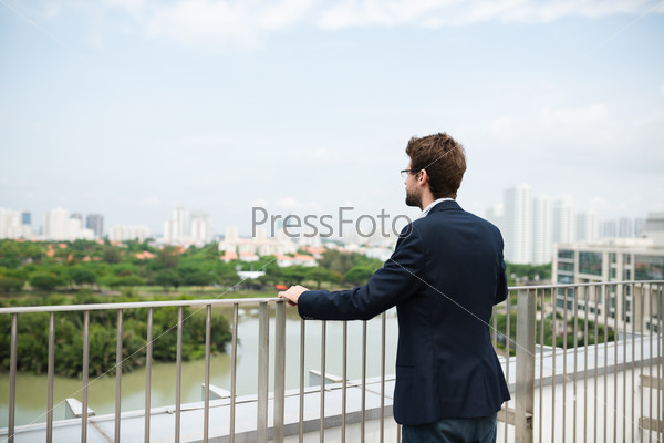 Businessman standing on balcony at looking at the city