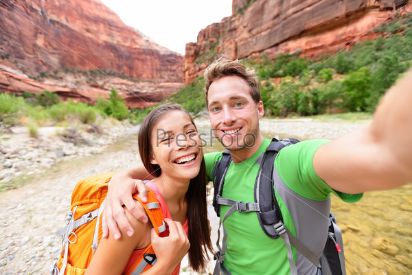 Travel hiking selfie self-portrait photo by happy couple on hike. Active lifestyle with hikers friends or lovers smiling at camera in Zion National Park, Utah, USA. Young Asian woman and Caucasian man