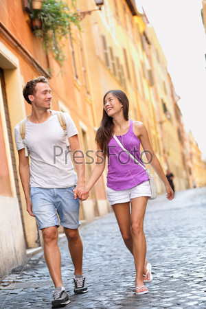 Young casual couple holding hands walking in Rome, Italy, Europe. Multiracial couple in love having fun laughing together. Asian woman, Caucasian man.