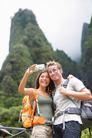 Couple taking selfie self portrait hiking on Hawaii in outdoor activity. Woman and man hiker taking photo with smart phone camera. Healthy lifestyle from Iao Valley State Park, Wailuku, Maui, USA.