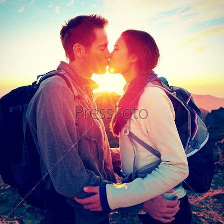 Kiss - couple kissing romantic at hiking sunset sharing embrace enjoying sunshine and love on beautiful hike in mountain nature landscape. Young interracial couple, Asian woman, Caucasian man in love.