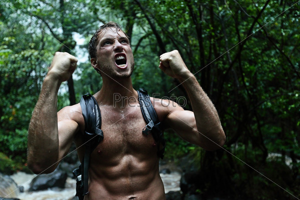 Muscular survivor man in jungle rainforest cheering aggressive. Strong male survival concept with guy celebrating cheerful in forest at night showing muscles and aggressive survival instincts.