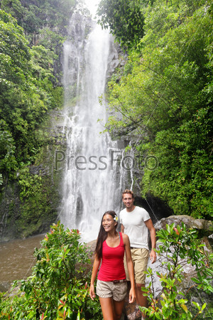 Hawaii tourist hiking people. Couple happy by waterfall during travel on the road to Hana on Maui, Hawaii. Ecotourism concept image with happy backpackers. Interracial Asian / Caucasian young couple.
