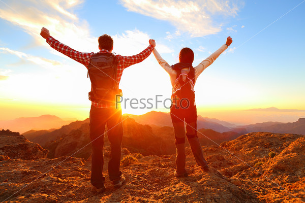 Freedom - Happy couple cheering and celebrating. Hiking man\
and woman raising arms excited in celebration outdoors. Hikers at\
sunset in mountain enjoying mountain top summit and success.