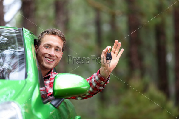 Car driver showing car keys and thumbs up happy. Young man holding car keys for new car. Rental cars or drivers licence concept with male driving in beautiful nature on road trip.
