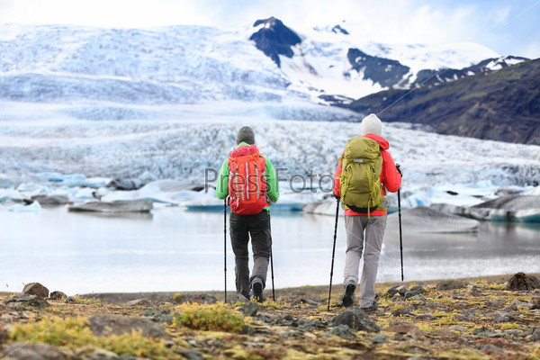 Hikers - people on adventure travel on Iceland. Hiking man man woman walking to glacier and glacial lagoon / lake of Fjallsarlon, Vatna glacier, Vatnajokull National Park. Couple in active lifestyle.