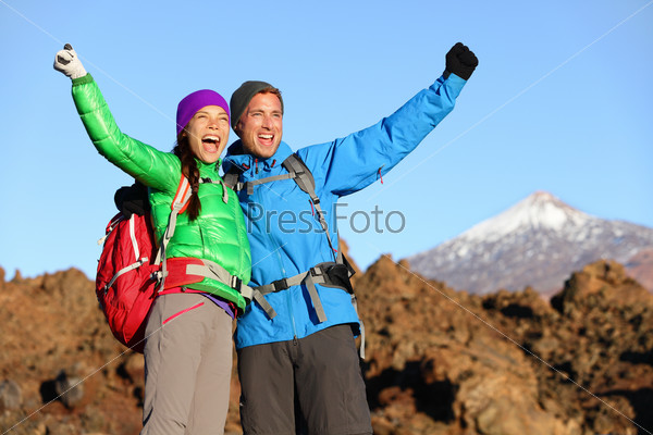 Happy celebrating winning hiking people at top. Cheering hiker couple enjoying freedom on hike with arms raised in mountain landscape. Woman and man on volcano Teide, Tenerife, Canary Islands, Spain