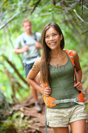 Happy hiker girl with backpack trekking in forest smiling.