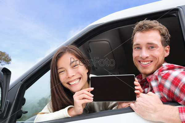 Tablet computer - couple driving in car showing screen with app or message. Young happy drivers on road trip. Asian woman, Caucasian man.
