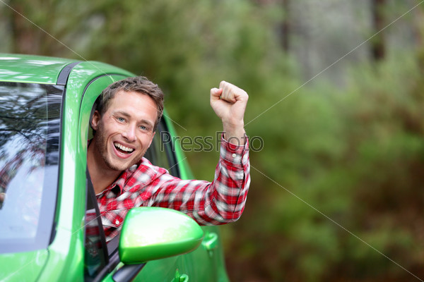 Green energy biofuel electric car driver happy and excited. Man driving new vehicle in cheerful in nature forest. Young male driver looking at camera with arm raised cheering.
