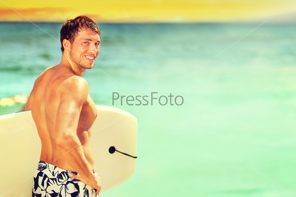 Surfer man going surfing on summer beach. Male bodyboarding surfing man good looking standing with bodyboard surfboard during vacation holidays getaway. Caucasian water sport model in his 20s.