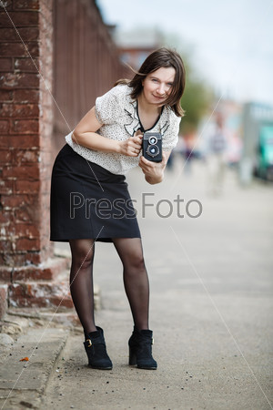Pretty young woman with an old vintage camera in hand on a background of an old brick wall. Retro style photo. Shallow depth of field. Selective focus on model. Vertical shot.