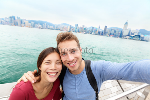 Selfie - Tourists couple taking selfportrait picture photo in Hong Kong enjoying sightseeing on Tsim Sha Tsui Promenade and Avenue of Stars in Victoria Harbour, Kowloon, Hong Kong. Travel concept.