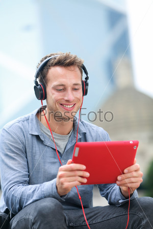 Video chat conversation. Man talking on tablet pc sitting outside using app on 4g wireless device wearing headphones. Casual young urban professional male in his late 20s.