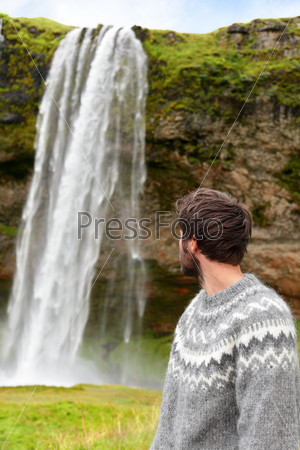 Icelandic sweater man by waterfall on Iceland outdoor smiling. Portrait of good looking male model  in nature landscape with tourist attraction Seljalandsfoss waterfall on Ring Road.