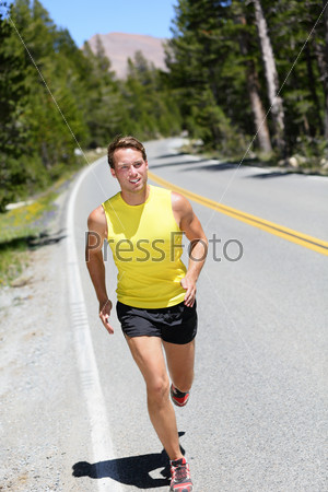 Running athlete man jogging on nature road in forest mountain. Full body male adult on a jog in summer.