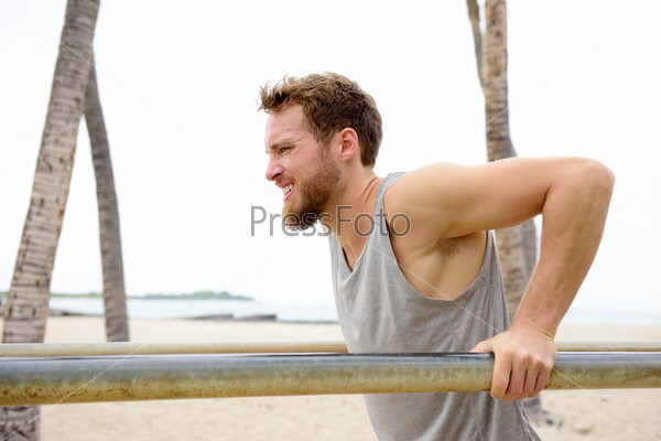 Cross fit man working out doing dips exercises strength training for arms outside on beach on fitness outdoor gym station.