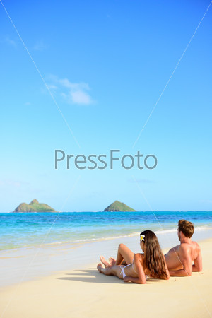 Beach vacations suntan couple relaxing in Lanikai, Oahu, Hawaii, USA. Vertical crop with blue sky copy space background for holiday vacation travel concept.