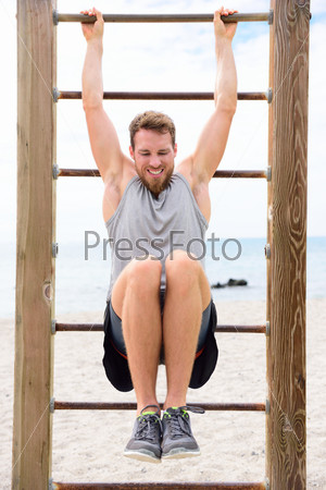 Fitness people - man training abs by lifting legs on cross fit bar rack outside on outdoor gym station.