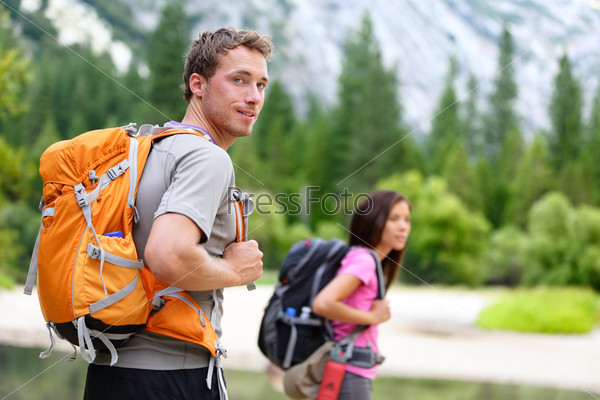 Hikers - people hiking, man looking at mountain nature landscape scenic with woman in background. Happy multicultural young couple in Yosemite National Park, California, USA