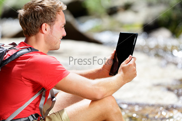 Tablet computer man hiker hiking in Yosemite, USA using travel app or map during hike, resting by river. Caucasian male hiker relaxing on a summer day.