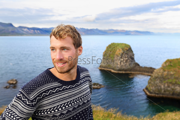 Fair isle sweater. Handsome man portrait in beautiful nature landscape. Young caucasian male model in his 20s smiling in by the ocean sea in Arnarstapi, Snaefellsnes, Iceland.