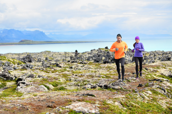 Exercise running sport. Runners on cross country trail run outdoors working out. Fit young fitness model man and asian woman training together outside in mountain nature on Snaefellsnes, Iceland.