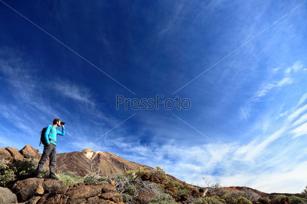 hiker in dramatic landscape hiking under deep blue sky looking in binoculars. Young Caucasian man during hike in Mountain landscape on volcano Teide, Tenerife, Canary Islands