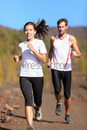 Young couple running together outdoors in beautiful volcanic landscape. Woman trail runner training for marathon run with male model jogging in background.