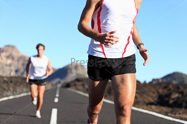 Running Sport. Runners on road in endurance run outdoors in beautiful landscape. closeup of man legs and torso with male runner in the background. Shallow DOF, focus on hips and arm.