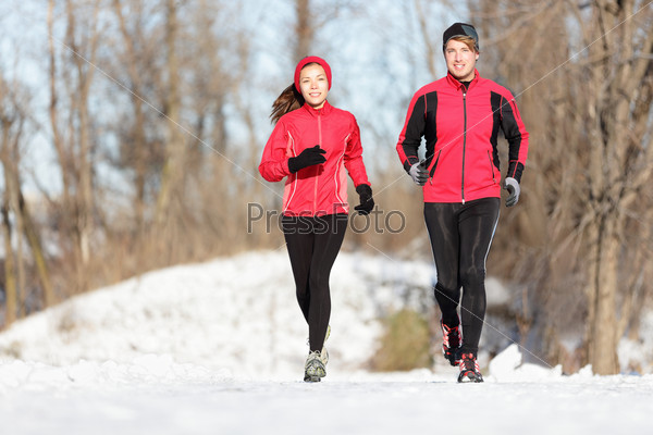 Sport couple running in winter. Runners jogging in snow in city park. Interracial young happy couple enjoying healthy lifestyle. Asian woman fitness model and caucasian man.