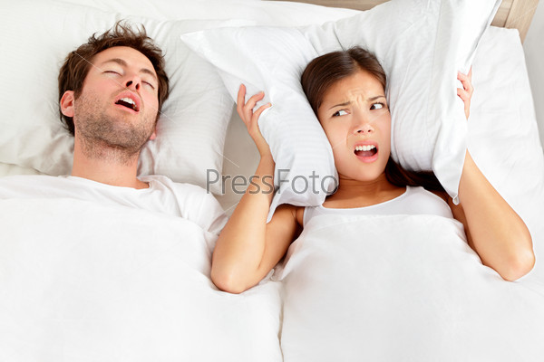 Snoring man. Couple in bed, man snoring and woman can not sleep, covering ears with pillow for snore noise. Young interracial couple, Asian woman, Caucasian man sleeping in bed at home.