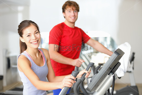 Fitness center people smiling happy working out on moonwalker fitness machines in fitness center. Asian woman, Caucasian man.