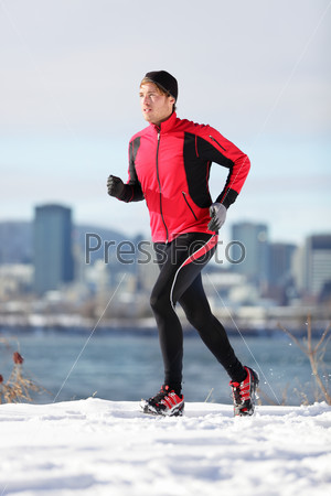 Fitness running man. Male runner training and jogging outdoors in winter snow with cityscape skyline. Workout and healthy lifestyle concept with Caucasian  fitness model in Montreal, Quebec, Canada.